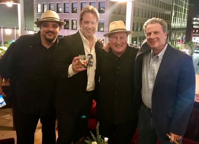 A group of guests toasting with cigars against a city skyline